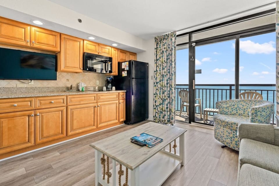 Unwind in this stylish 11th-floor oceanfront living room, where beach views meet modern comfort. A spacious balcony, sleek smart TV, and inviting seating create the perfect retreat. The open layout flows into a fully stocked kitchen and dining area.