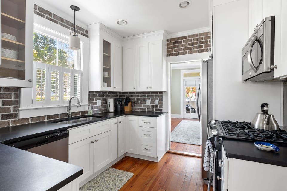 This modern kitchen features stainless steel appliances, black countertops, and exposed brick accents for a cozy yet upscale feel.