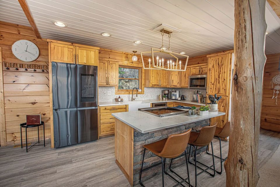 Rustic-Modern Kitchen with High-End Finishes – This stunning kitchen combines the warmth of natural wood with sleek modern appliances, an oversized island with seating for three, and chic pendant lighting, making it perfect for entertaining.