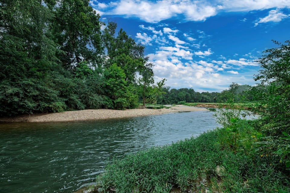 The riverside access area beside the home offers a grassy approach to the calm water and rocky shoreline.