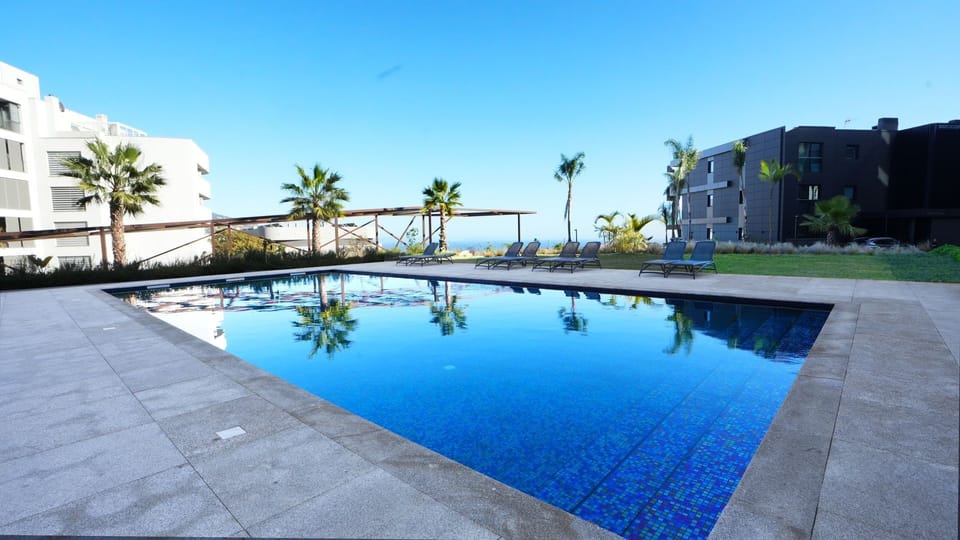 Large shared pool in a modern complex, surrounded by lush greenery and stylish sun loungers. A perfect retreat for relaxation under the Madeira sun #outdoorpool #funchal