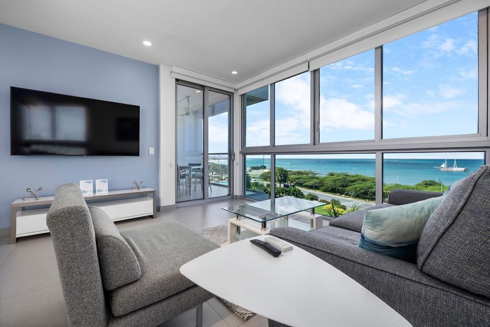 Sink into your sofa and watch sailboats drift across turquoise waters, framed by lush coastal greenery—your peaceful seaside escape awaits.