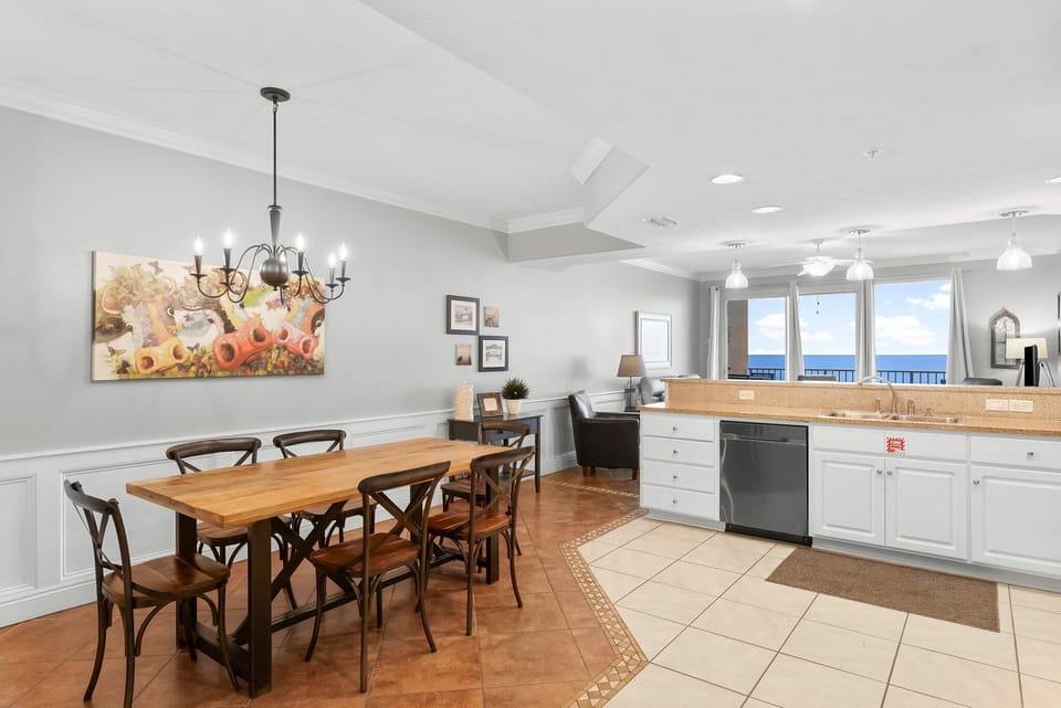 Dining area with rustic wooden table adjacent to a kitchen featuring ocean views.