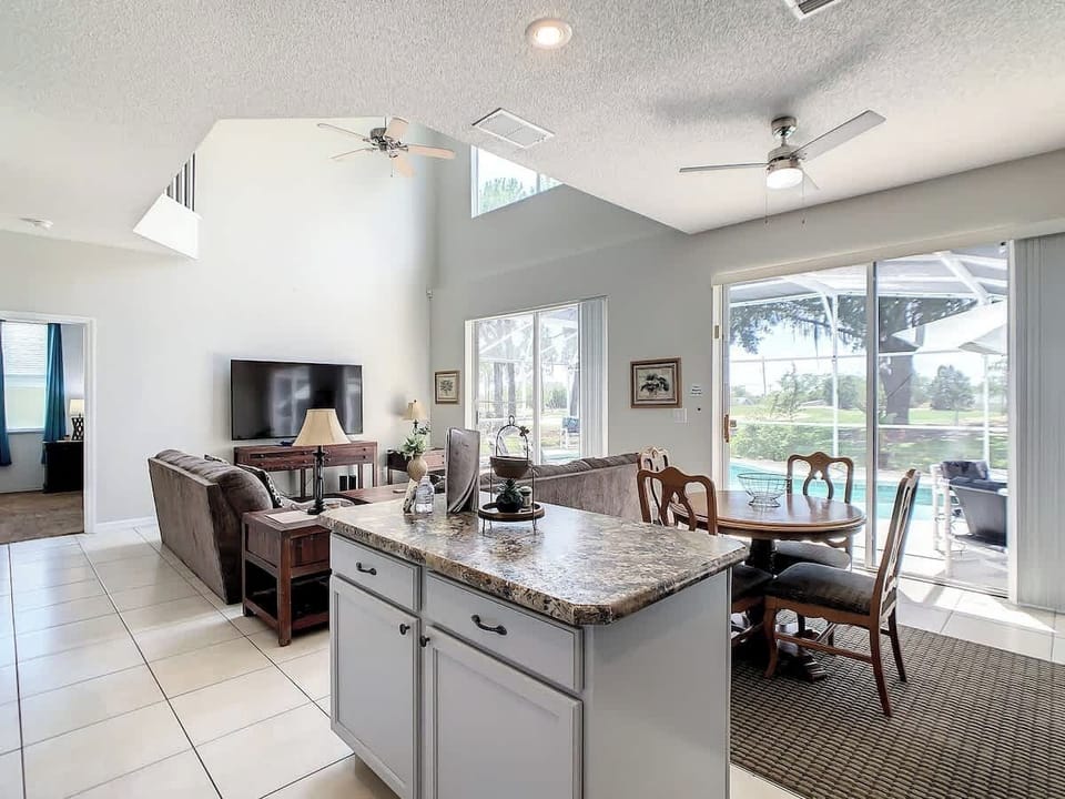 Bright and spacious open-concept kitchen with granite countertops, a four-seat dining table, and a seamless flow into the living area and poolside patio.