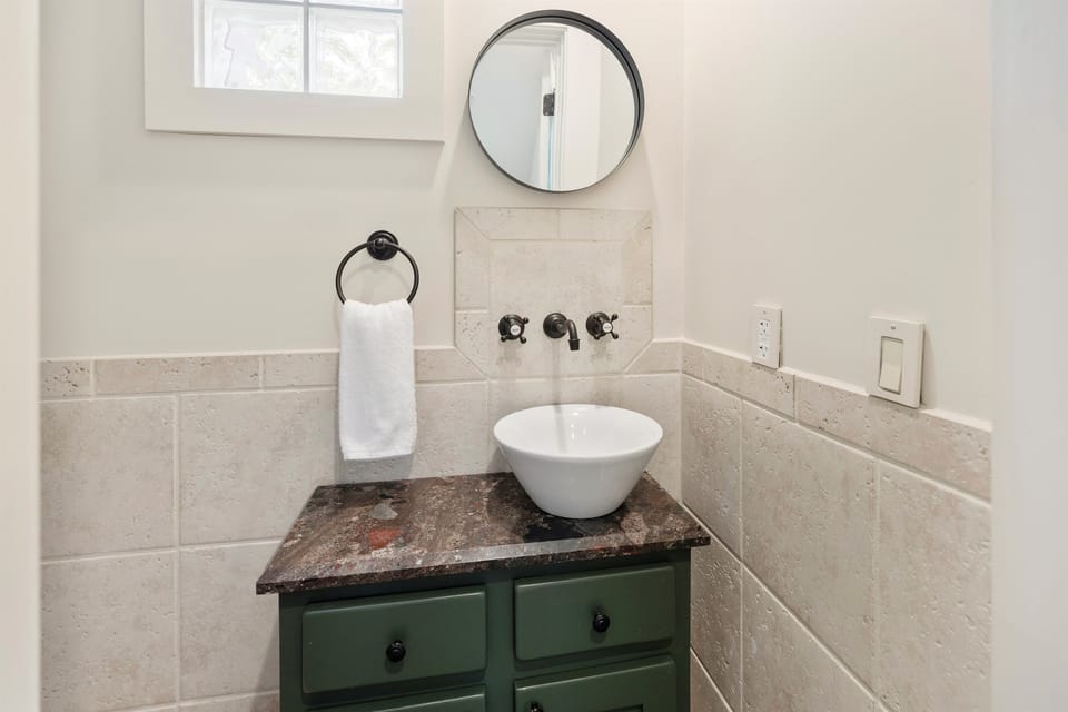 Refresh in your charming powder room featuring a striking vessel sink, elegant stone countertop, and warm natural light streaming through the window.