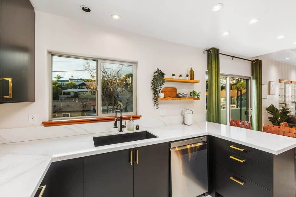 This stylish kitchen boasts sleek black cabinets, marble countertops, and modern appliances. Large windows bring in natural light, while open shelving adds charm. Perfect for cooking and entertaining, with seamless flow to the dining area.