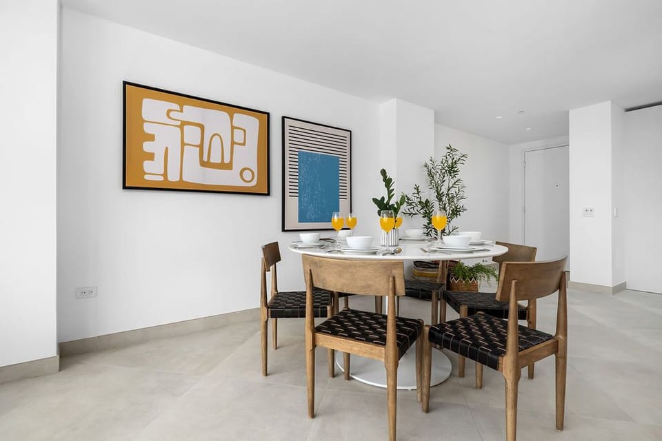 Picture yourself sharing meals around this stylish dining table, where bold modern art meets natural wood warmth. The bright, airy space invites you to linger over breakfast or evening conversations.