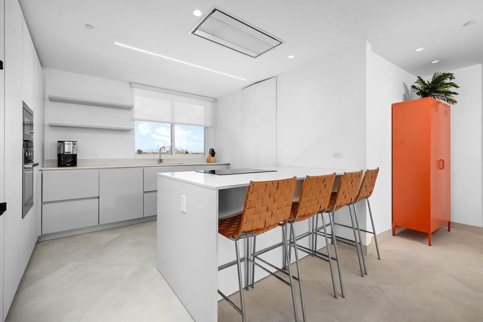 This sleek, modern kitchen features plenty of counter space for meal prep, a bright island with comfortable seating, and stylish pops of color to brighten your stay.
