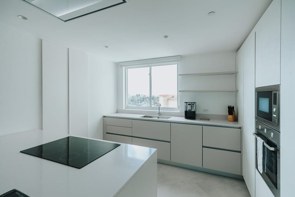 You'll love preparing meals in this sleek, modern kitchen with gleaming countertops, a spacious island with a cooktop, built-in appliances, and soft natural light streaming through the window.