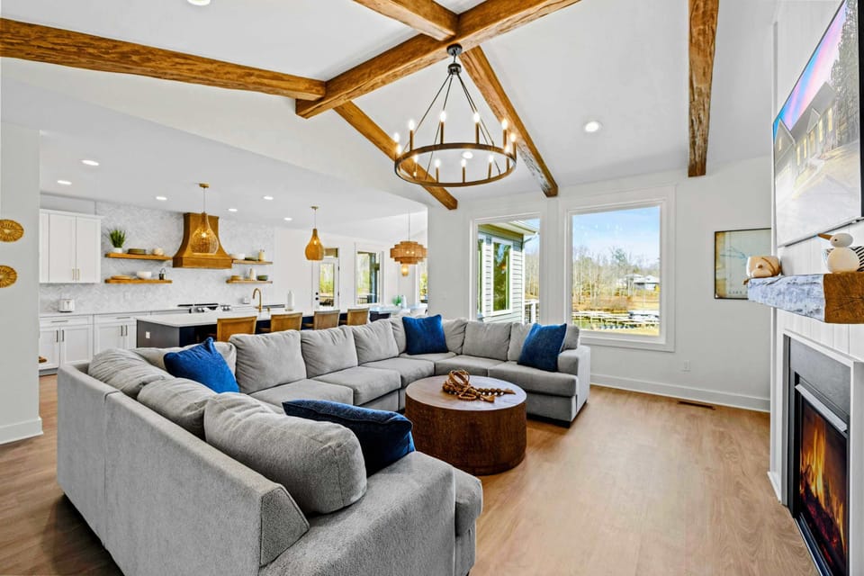 Great Room - Vaulted ceilings and reclaimed wood beams crown an open layout, with a wall of windows framing the lake and a fireplace for easy evenings in.