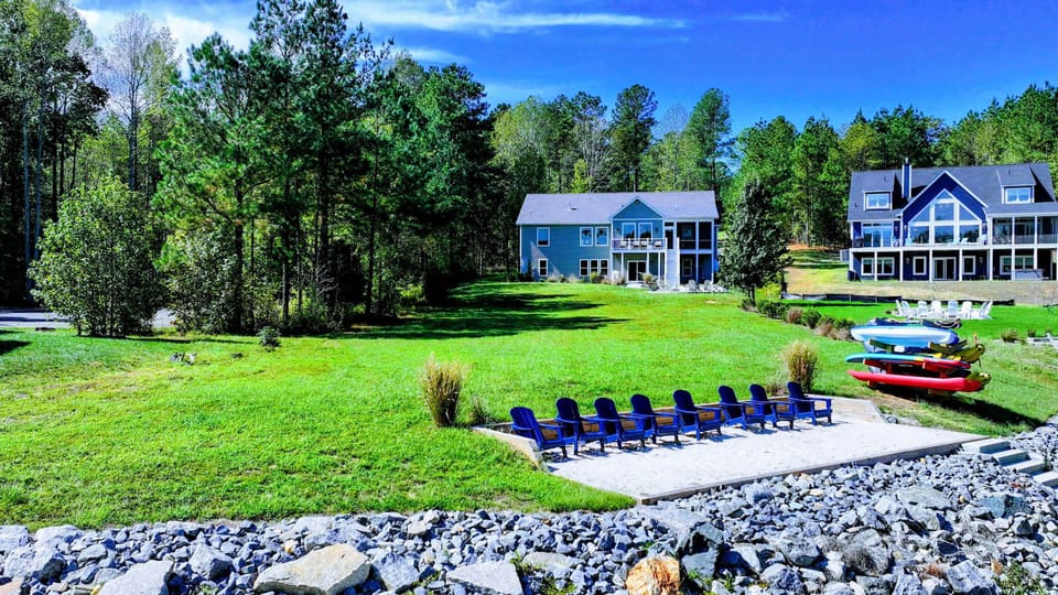 Backyard - A wide lakefront lawn rolls down to the fire pit and a long row of Adirondack chairs, with the kayak rack ready at the shore.