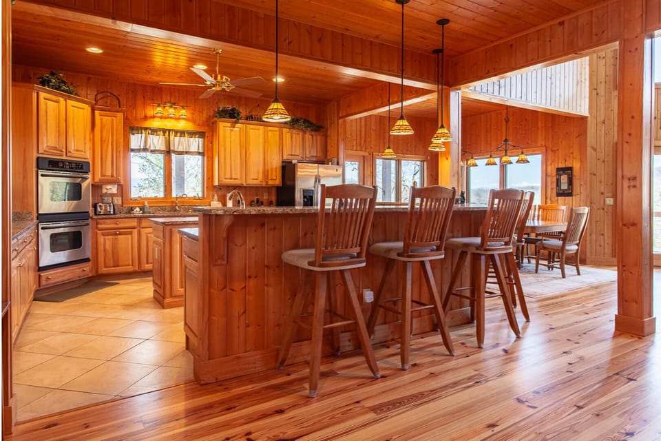 Spacious kitchen featuring wood cabinetry, granite countertops, breakfast bar seating, and adjacent dining area. Open-concept layout with vaulted wood ceilings.