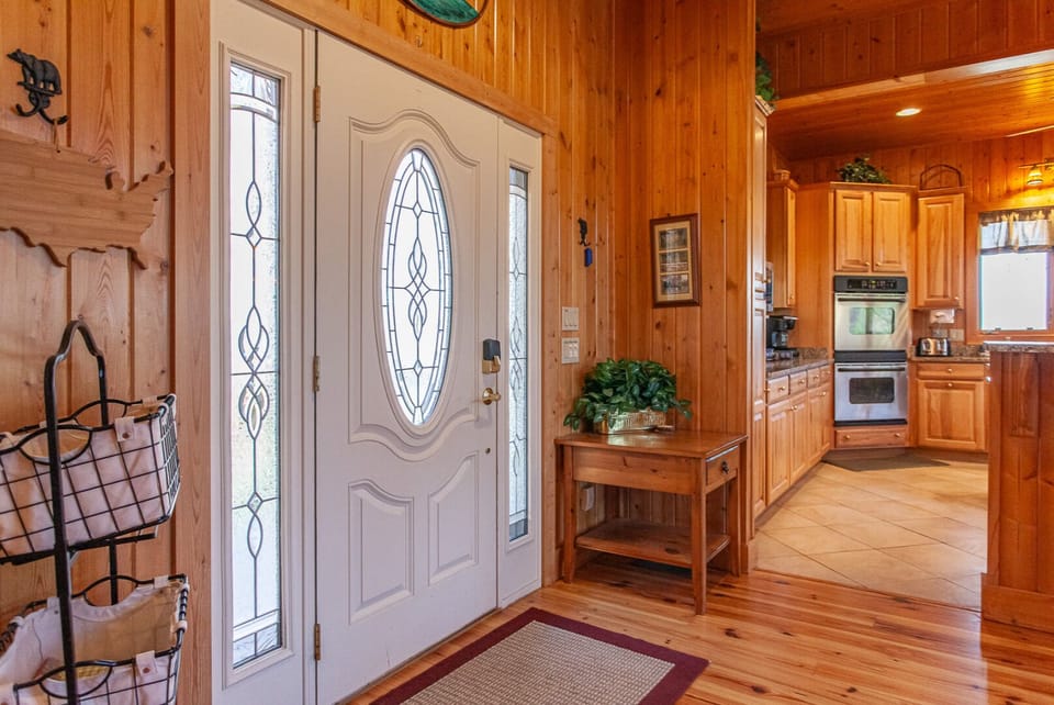 Wood-lined foyer opening into the spacious kitchen with natural wood cabinetry and hardwood flooring. Bright entry leading into the main living area.
