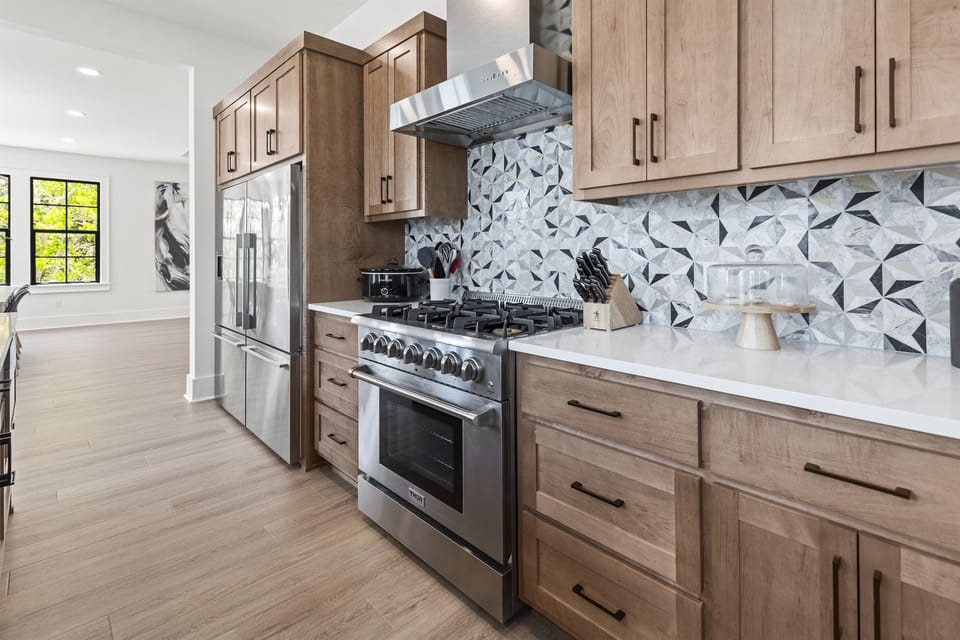 Your gourmet kitchen features warm wood cabinets, geometric marble backsplash, and premium stainless steel appliances for memorable meal preparation.