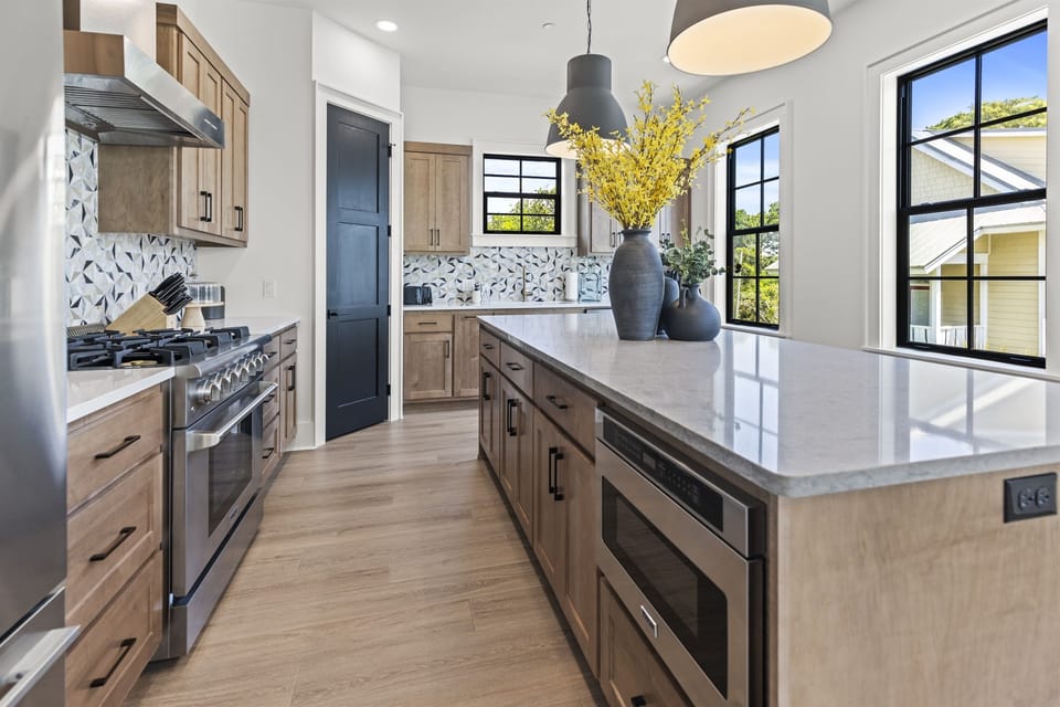 Your spacious kitchen invites culinary adventures with gleaming quartz counters, modern appliances, and abundant natural light streaming through black-framed windows.