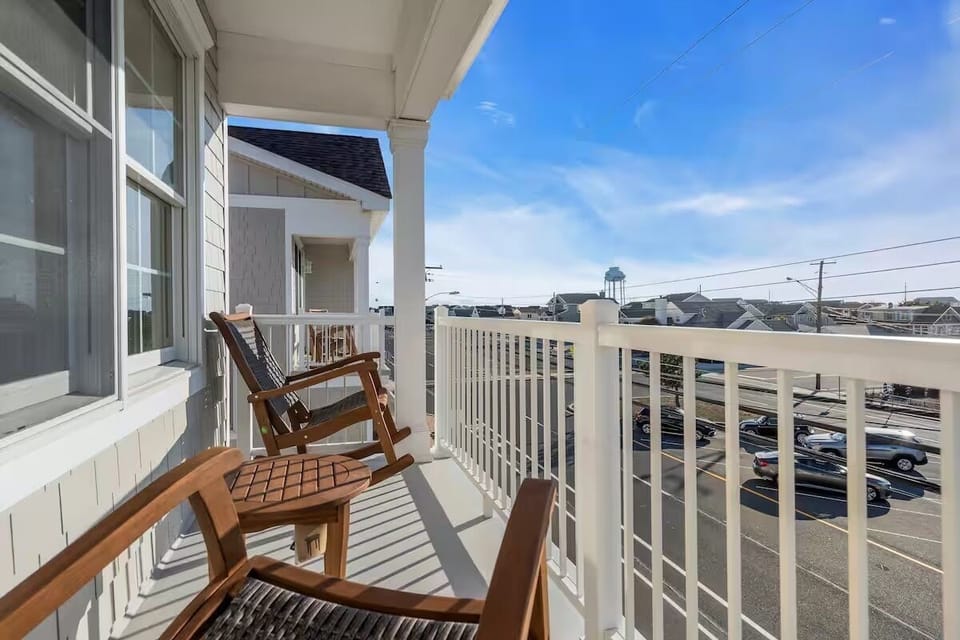 Open second-floor balcony with wood-armed rocking chair, white wood railing, and open-sky neighborhood views.