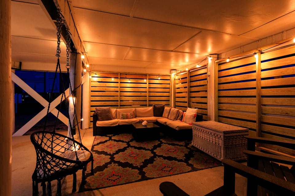 A cozy, dimly lit outdoor patio featuring a sectional sofa, patterned rug, and warm string lights.