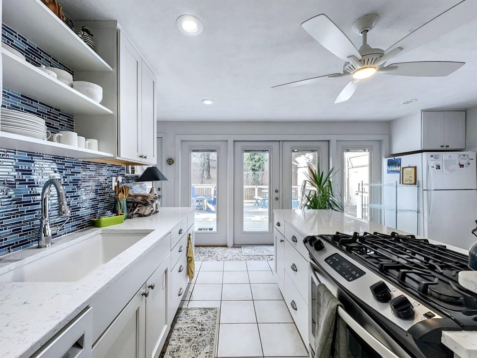 Modern kitchen featuring open shelving, stylish blue backsplash, and plenty of counter space.