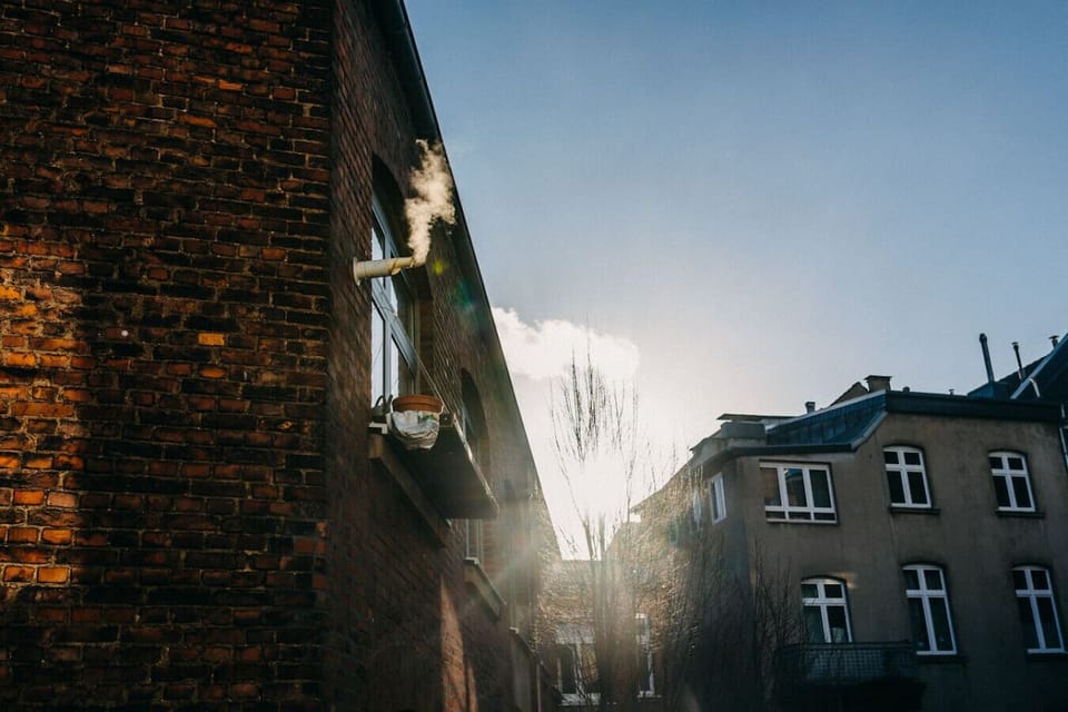 Morgenstimmung im Hinterhof – Sonnenstrahlen brechen durch die alten Backsteinmauern, während der Dampf sanft in die kühle Luft aufsteigt. Ein urbaner Rückzugsort mit historischem Charme.