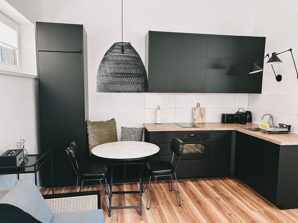 Stilvolle Küche | Schwarze Fronten, warmes Holz & Designerleuchten – diese Küche verbindet modernes Design mit Funktionalität. Perfekt ausgestattet für kulinarische Erlebnisse in deinem Zuhause auf Zeit!