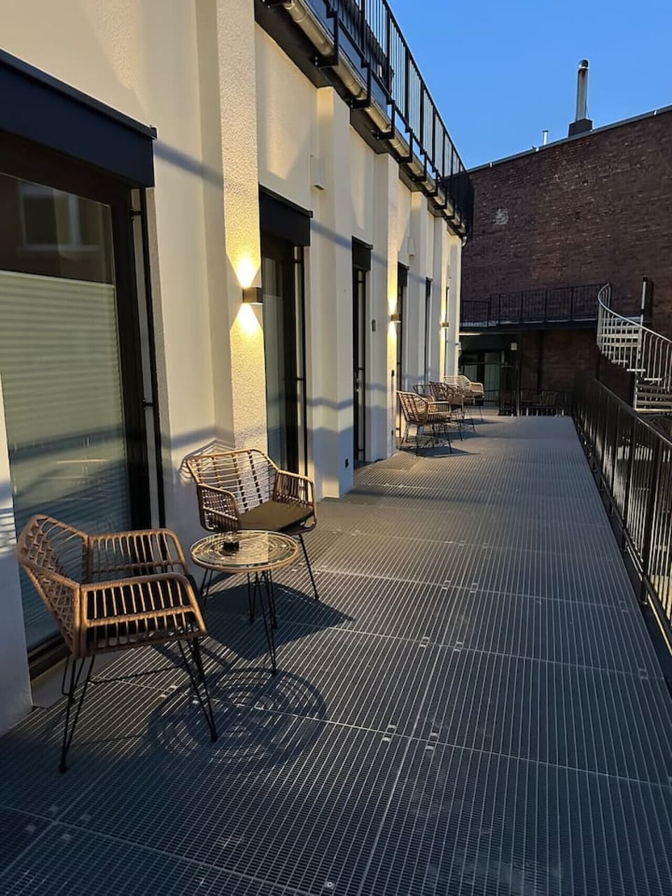 Ein lauer Abend auf dem Balkon – warme Beleuchtung, stilvolle Rattanmöbel und ein urbanes Flair machen diesen Außenbereich zu einem perfekten Ort für entspannte Stunden unter freiem Himmel.
