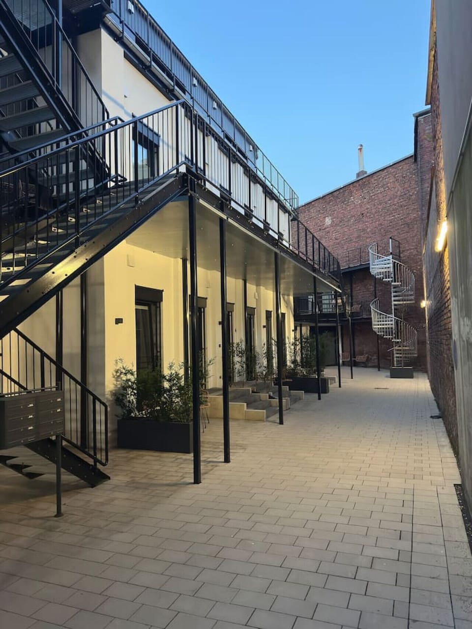 Ein stilvoller Innenhof mit industriellem Charme: Die modernen Loft-Apartments treffen auf elegante Metalltreppen und warmes Licht – ein urbanes Refugium für Designliebhaber und Stadtentdecker.