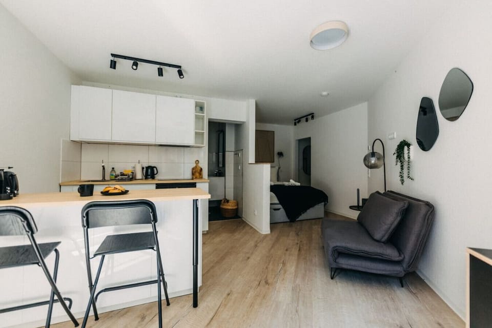 Ein Ort zum Ankommen und Wohlfühlen – das gemütliche Sofa mit stilvollen Kissen lädt zum Entspannen ein, während große Fenster den Raum mit Tageslicht fluten und den Blick auf die charmante Backsteinfassade freigeben.