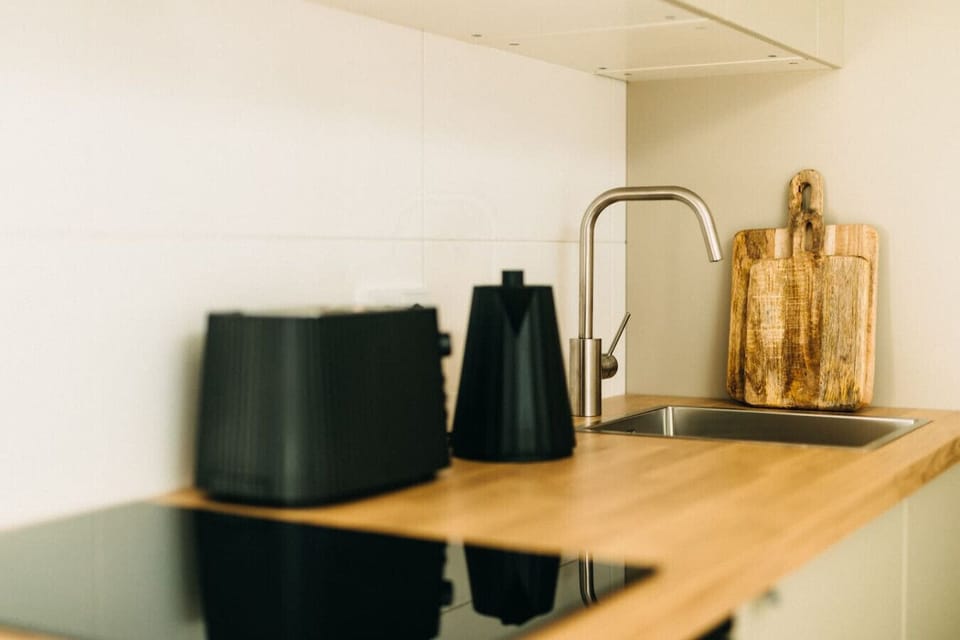 Moderne Eleganz trifft natürliche Wärme: Die stilvolle Küche mit Holzarbeitsplatte, Designer-Wasserkocher und hochwertigen Geräten lädt zum Kochen ein. Perfekt für ein entspanntes Frühstück oder ein selbstgemachtes Dinner mit Blick auf die Stadt.
