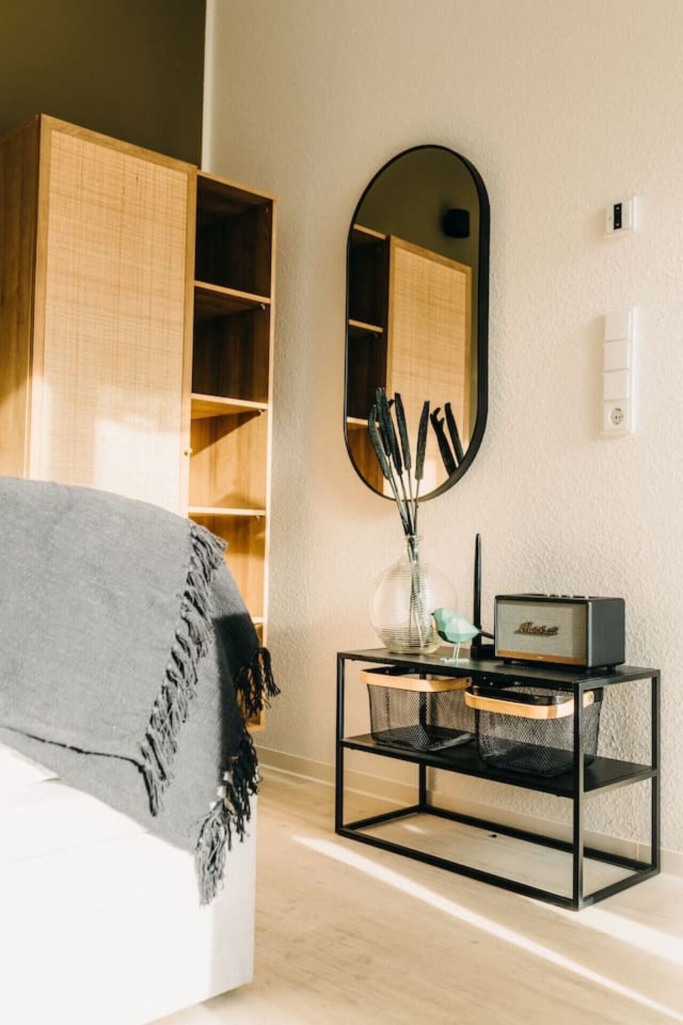 Ein stilvoller Mix aus Funktionalität und Ästhetik: Der Rattanschrank bietet viel Stauraum, während der elegante Spiegel und das minimalistische Sideboard mit Deko-Elementen eine harmonische Atmosphäre schaffen.