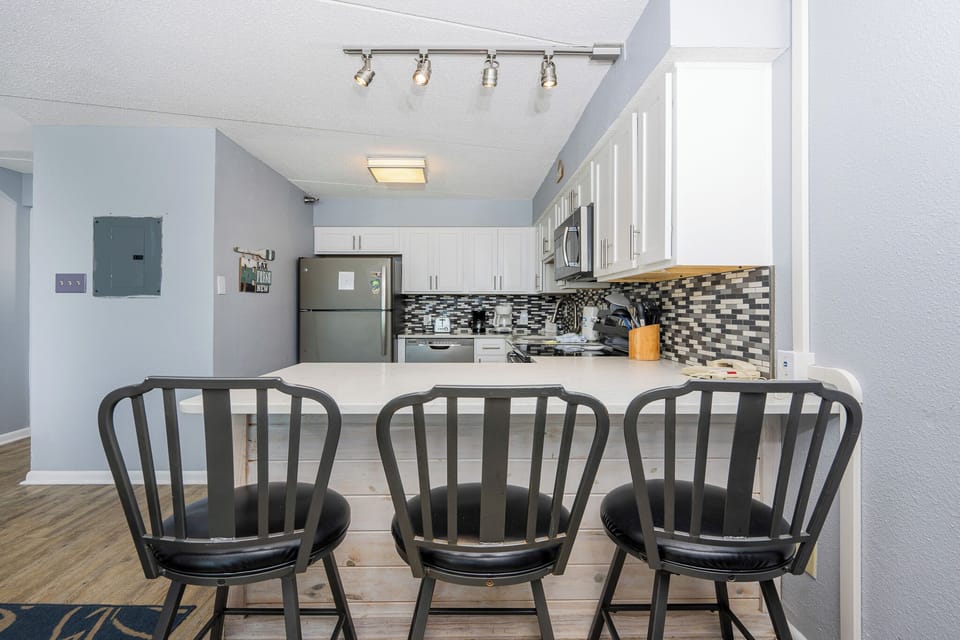 This kitchen features sleek white cabinetry, stainless appliances, and a stylish bar area with black stools for casual dining