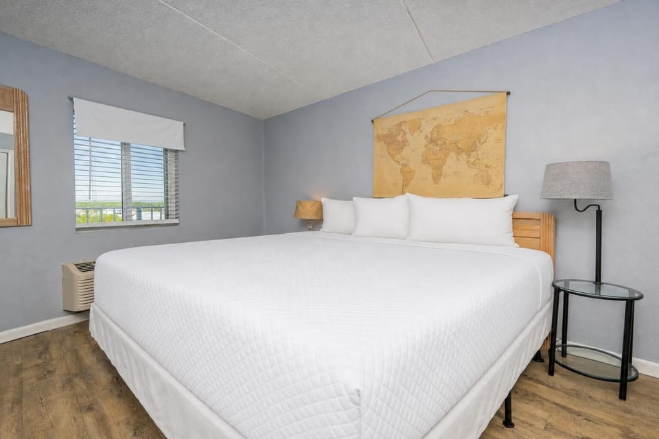 This bedroom features a large bed with crisp white linens, a stylish map decor, and a sunny view through the window