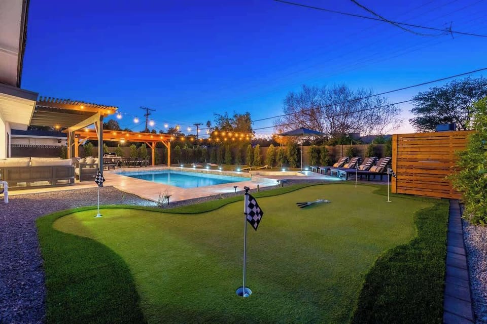A spacious backyard retreat with resort-style pool, professional putting green, and poolside lounge area under ambient string lights—perfect for evening relaxation and friendly competition.
