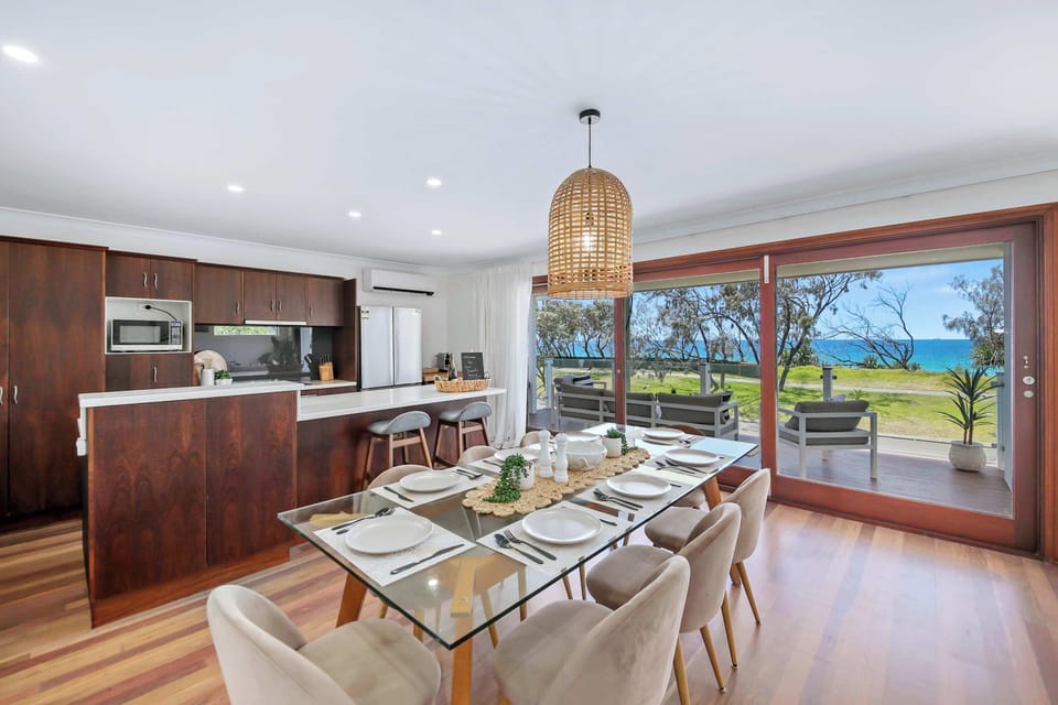 The open plan dining area offers a sleek glass table, seating for eight, with additional seating at the kitchen island, and sparkling waterfront views.
