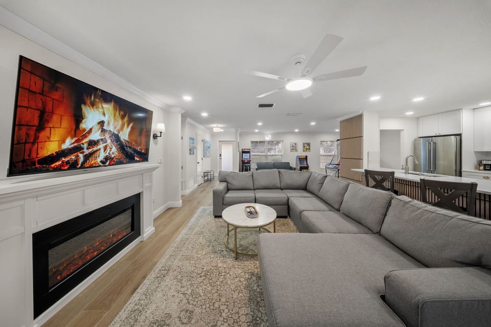 The living room has an electric fireplace, flat screen TV, and multiple seats.