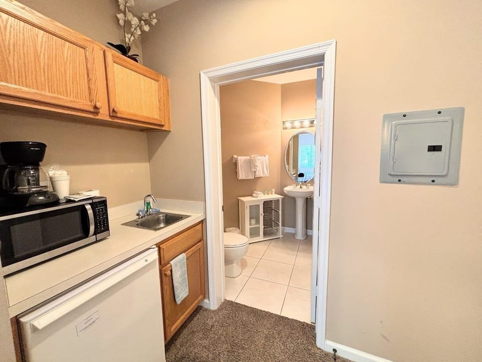 Functional kitchenette space with microwave, mini fridge, sink, coffee maker, and easy access to the bathroom.