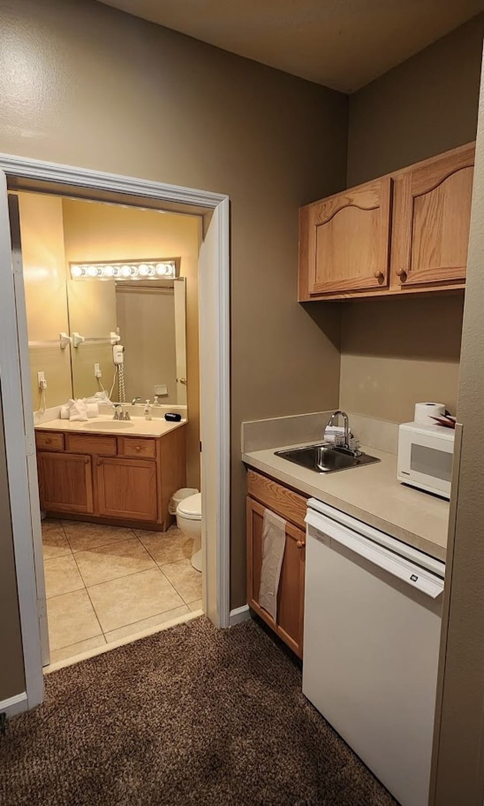 Convenient kitchenette area with sink, microwave, cabinet storage, and easy access to the bathroom.