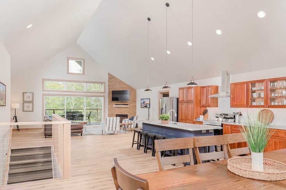 Open concept dining area, kitchen, & living room with stairs leading to front door. Kitchen features stainless steel appliances including a french door refrigerator & a glass cooktop stove. The both the dining room table and the island seats 8 