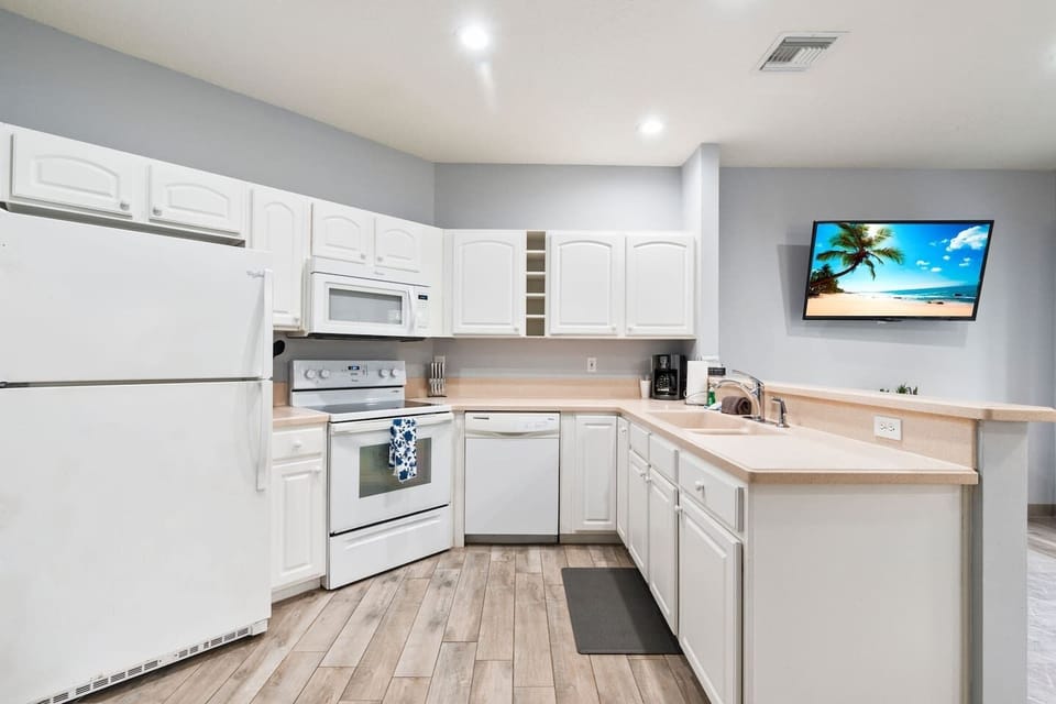 Bright kitchen with white cabinetry, full-size appliances, breakfast bar, and an open layout connecting to the living area.