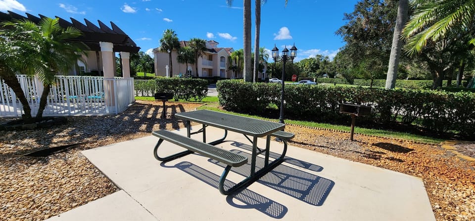 Outdoor picnic area with shaded seating and landscaped surroundings near the community pool.