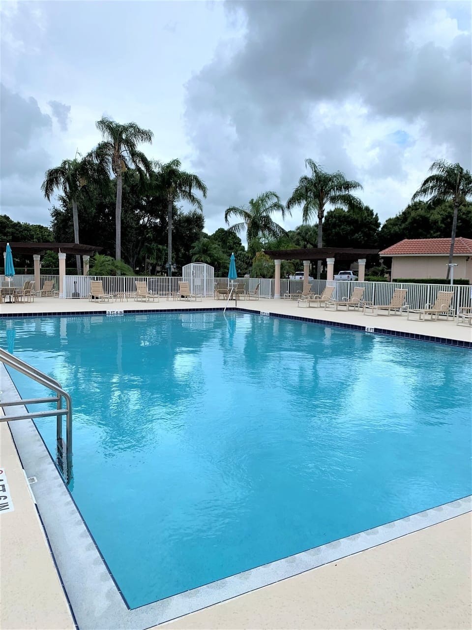 Bright community pool with lounge seating, umbrellas, and a peaceful Florida setting.