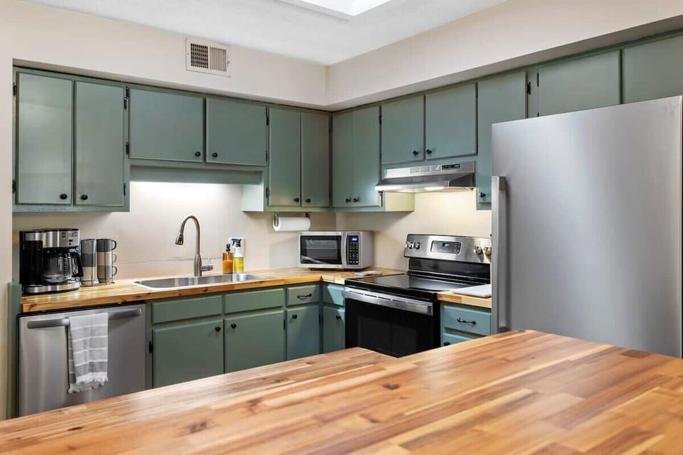 Inviting kitchen with sage green cabinets, stainless steel appliances, and warm wood countertops. A bright and functional space that makes cooking easy and enjoyable.