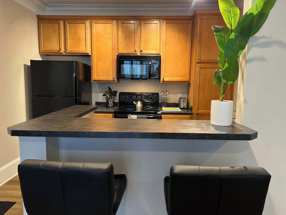 Modern kitchen with warm wood cabinetry, black appliances, and a breakfast bar with seating. A great space for casual meals, morning coffee, or planning your day.