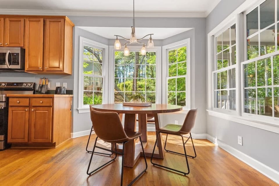 This cozy breakfast nook is surrounded by large windows that flood the space with natural light. It is a perfect spot to start your morning while enjoying views of the lush outdoor greenery.
