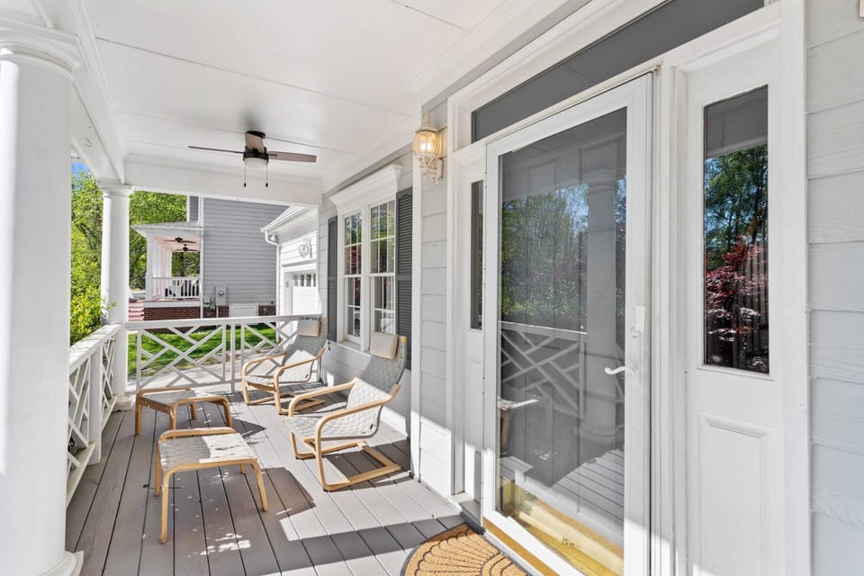 The inviting entryway boasts a spacious deck with modern chairs and stylish white columns. Large windows and a glass door flood the interior with light while providing a seamless transition to the outdoors.