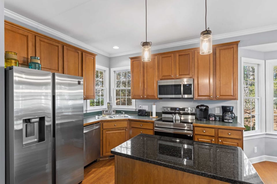 Modern chef's kitchen featuring stainless steel appliances and ample honey-toned wood cabinetry. The dark granite countertops and spacious island offer plenty of prep space for home-cooked meals during your stay.