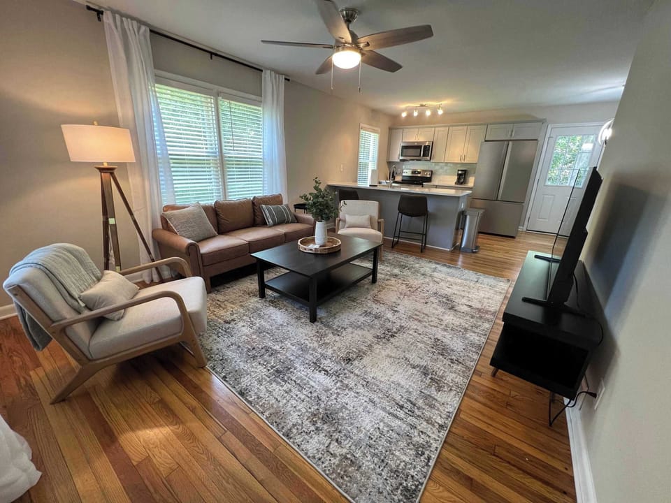 Inviting open living space with comfortable seating, soft area rug, and warm wood floors. The living room flows into a bright kitchen with island seating, creating a welcoming place to relax, gather, and feel right at home.