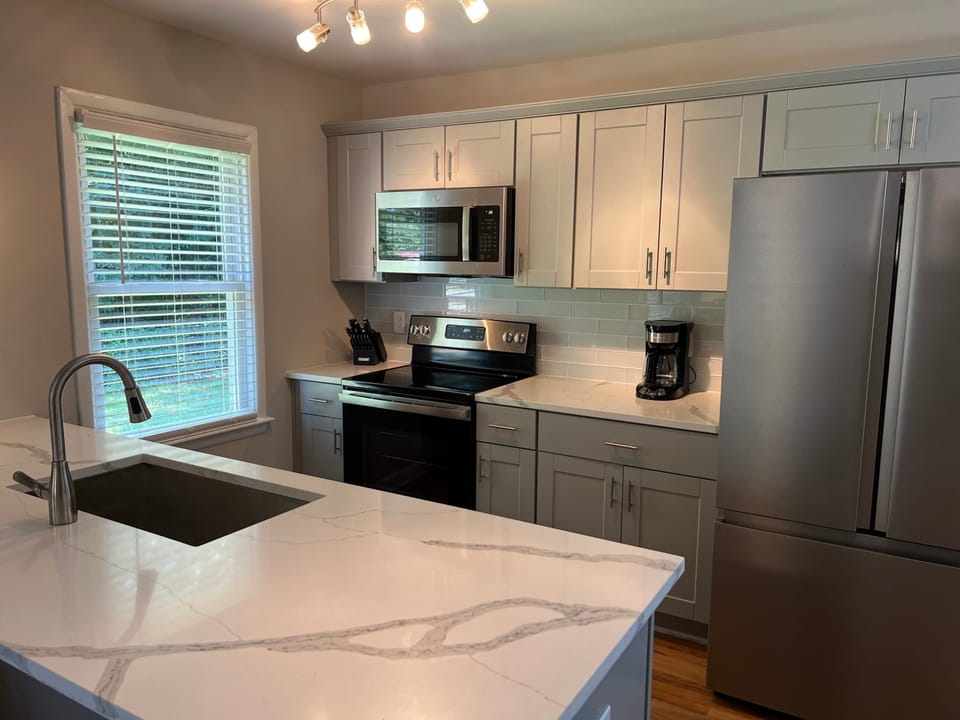 Bright, modern kitchen with sleek stainless steel appliances, quartz countertops, and ample cabinet space. Enjoy cooking with a large island, contemporary lighting, and natural light from the window perfect for comfortable, extended stays.