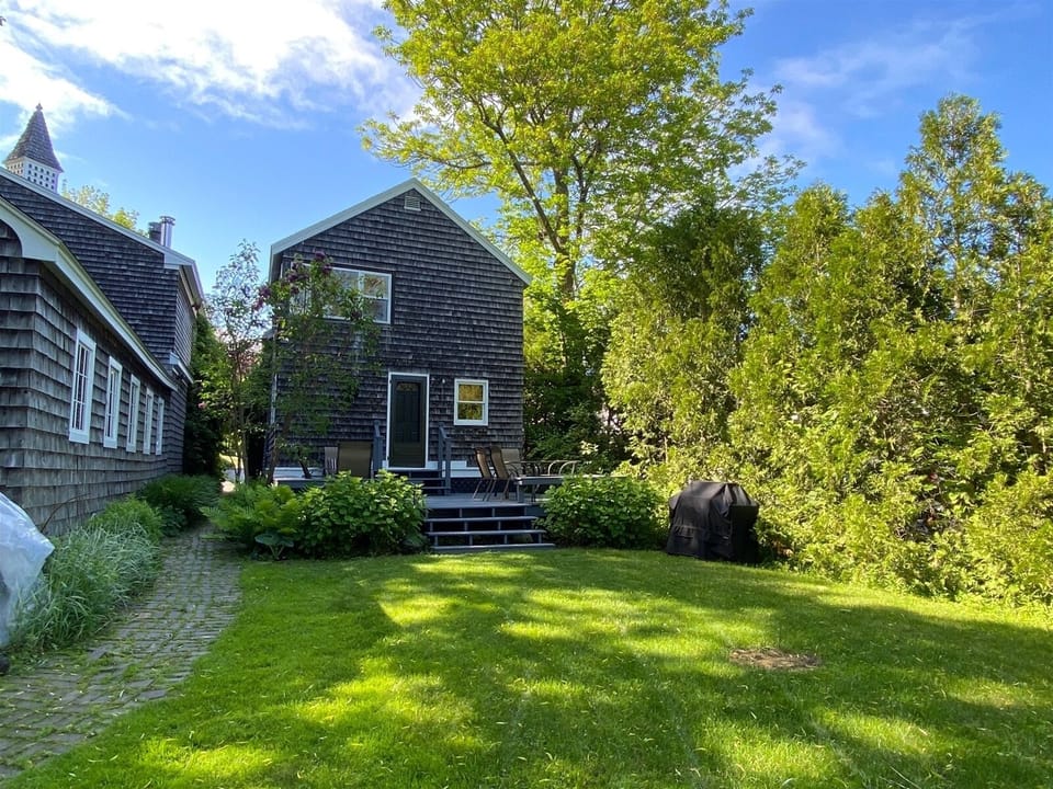 The rear of the cottage has a deck with dining area, gas grill, and a small lawn