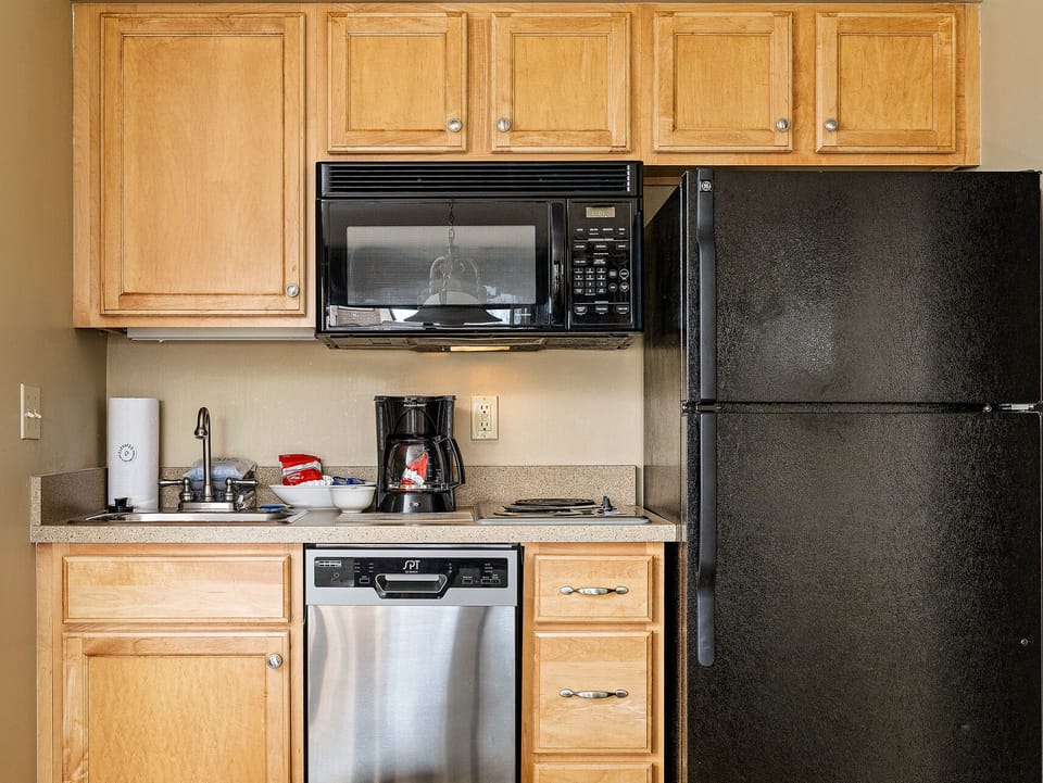 Compact kitchenette w/ wood cabinets, full-size fridge & essentials for easy meals.