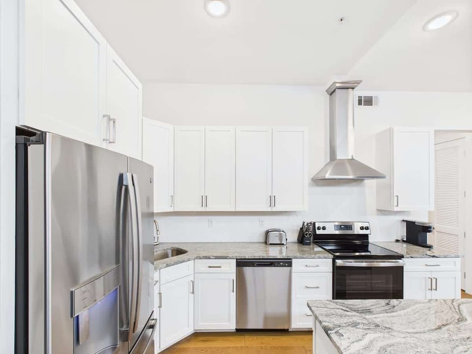 The fully equipped modern kitchen features culinary essentials, stainless steel appliances, and island bar seating.